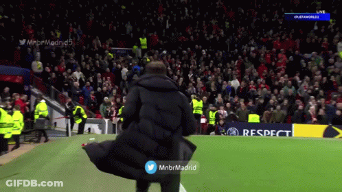 A Man In A Black Coat Stands On A Soccer Field In Front Of A Crowd GIF