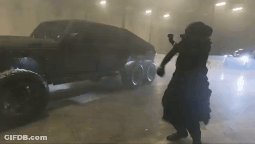 A Man In A Black Dress Is Dancing In Front Of A Car . GIF