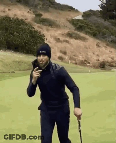 A Man In A Black Hat Is Holding A Golf Club On A Golf Course . GIF