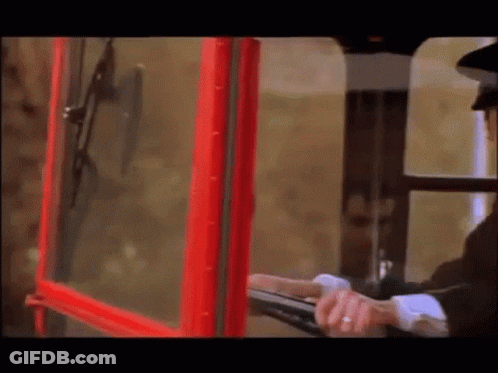 A Man In A Black Hat Is Looking Out Of A Red Telephone Booth GIF