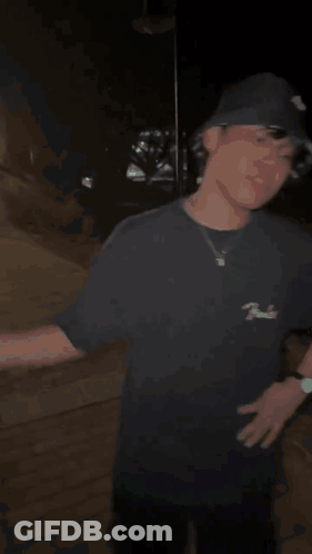 A Man In A Black Hat Is Shaking Hands With Another Man In A Dark Room . GIF