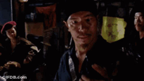 A Man In A Black Hat Is Standing In A Dark Room With A Group Of People . GIF