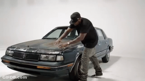 A Man In A Black Hat Is Standing Next To A Car GIF