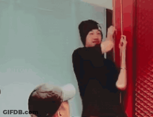 A Man In A Black Hat Is Standing Next To A Red Door . GIF