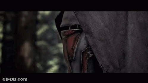 A Man In A Black Hood Is Holding A Red Light Saber In A Dark Forest GIF