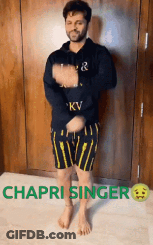 A Man In A Black Hoodie And Yellow Shorts Is Dancing In Front Of A Wall . GIF