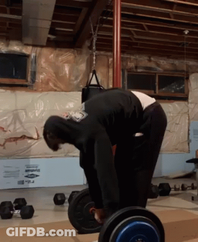 A Man In A Black Hoodie Is Bending Over To Lift A Barbell In A Gym GIF