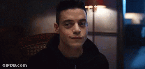 A Man In A Black Hoodie Is Sitting In A Chair And Smiling At The Camera . GIF