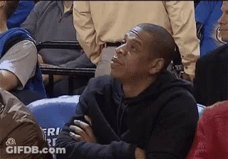 A Man In A Black Hoodie Is Sitting In A Crowd Of People Watching A Game . GIF