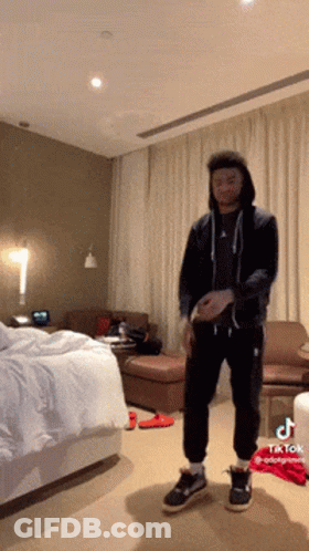 A Man In A Black Hoodie Is Standing In A Hotel Room With Tiktok Written On The Bottom GIF