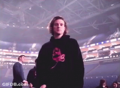 A Man In A Black Hoodie Is Standing In Front Of A Sign That Says To A Construction Area GIF