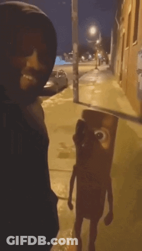A Man In A Black Hoodie Is Standing Next To A Cartoon Character On The Sidewalk GIF