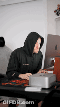 A Man In A Black Hoodie Is Typing On A Laptop GIF