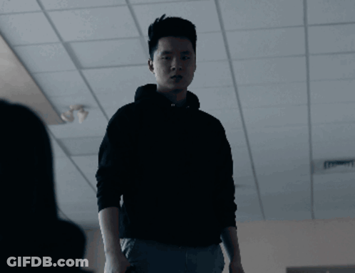 A Man In A Black Hoodie Stands In A Dark Room With The Word Sure Behind Him GIF