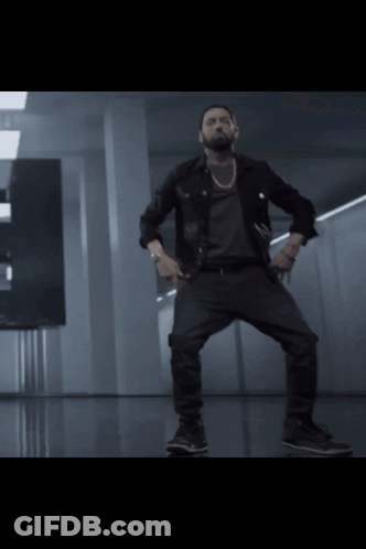 A Man In A Black Jacket And Black Pants Is Dancing In A Dark Room GIF