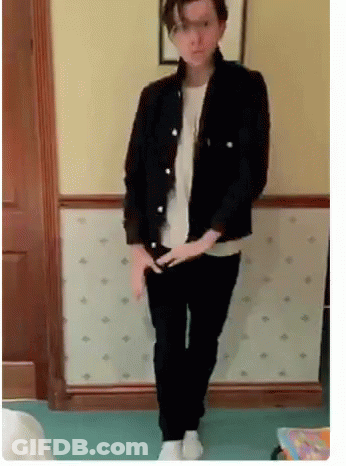 A Man In A Black Jacket And Black Pants Is Standing In Front Of A Wall . GIF