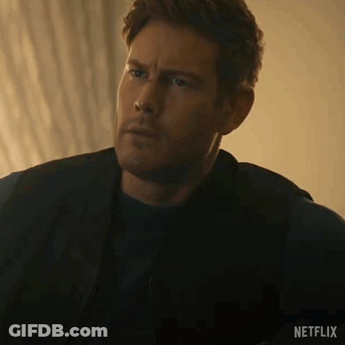 A Man In A Black Jacket And Black Shirt Is Sitting On A Couch And Looking At The Camera . GIF