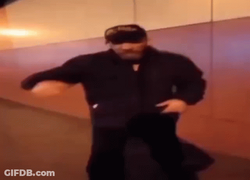 A Man In A Black Jacket And Hat Is Dancing In A Hallway . GIF