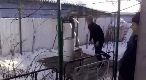 A Man In A Black Jacket And Hat Is Standing In The Snow GIF