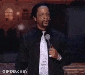 A Man In A Black Jacket And Tie Is Holding A Microphone And Giving A Speech . GIF