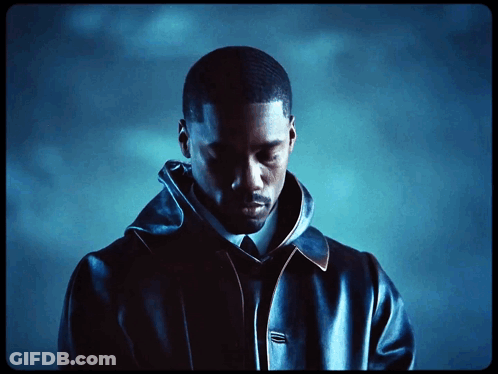 A Man In A Black Jacket And Tie Looks Down At Something GIF