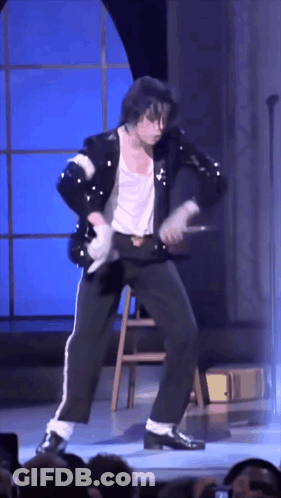 A Man In A Black Jacket And White Pants Is Dancing On Stage GIF
