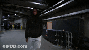 A Man In A Black Jacket And White Pants Is Walking Through A Dark Room GIF