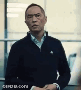 A Man In A Black Jacket And White Shirt Is Standing In Front Of A Window And Making A Funny Face . GIF