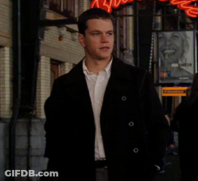 A Man In A Black Jacket And White Shirt Is Walking Down A Street In Front Of A Sign That Says ' Coca Cola ' GIF