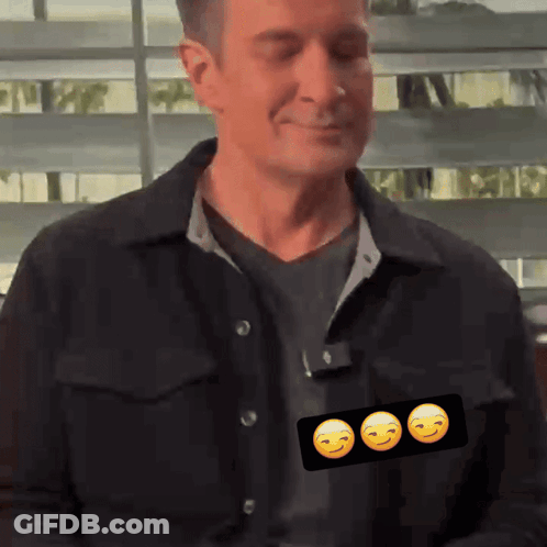 A Man In A Black Jacket Has Three Smiley Faces On His Shirt GIF