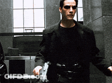 A Man In A Black Jacket Holds A Gun GIF