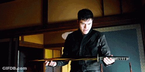 A Man In A Black Jacket Holds A Large Sword In His Hands GIF