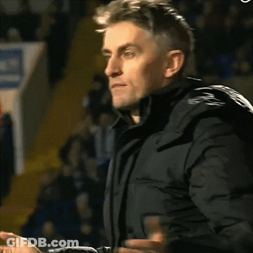 A Man In A Black Jacket Is Clapping His Hands In A Crowd GIF