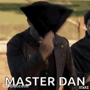 A Man In A Black Jacket Is Covering His Face With A Black Hat And Says `` Master Dan '' . GIF