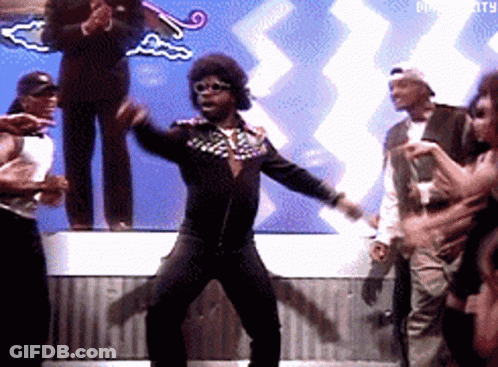 A Man In A Black Jacket Is Dancing In Front Of A Crowd With The Word Diversity In The Background GIF