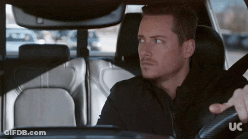 A Man In A Black Jacket Is Driving A Car With The Letters Uc On The Steering Wheel GIF