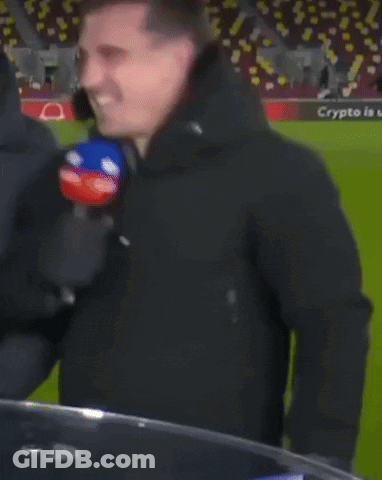 A Man In A Black Jacket Is Holding A Microphone In Front Of A Soccer Field That Has The Word Qatar On It GIF