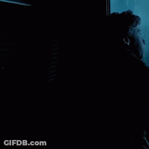 A Man In A Black Jacket Is Looking Out A Window With His Hand On The Glass GIF