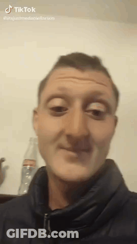A Man In A Black Jacket Is Making A Funny Face In Front Of A Bottle Of Soda . GIF