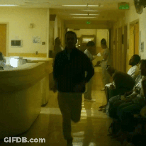 A Man In A Black Jacket Is Running Down A Hallway GIF