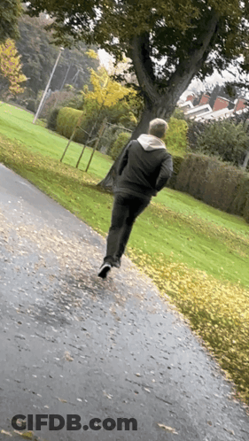 A Man In A Black Jacket Is Running Down A Path GIF