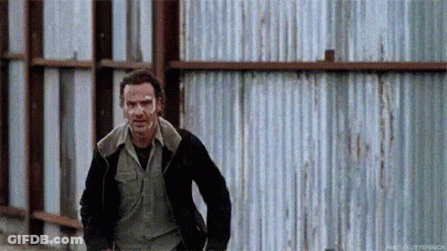 A Man In A Black Jacket Is Running In Front Of A Metal Fence . GIF