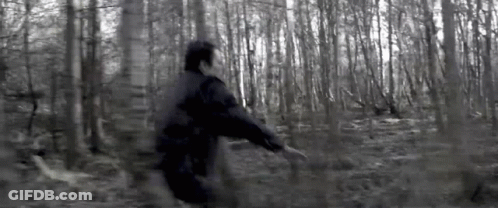 A Man In A Black Jacket Is Running Through A Dark Forest . GIF