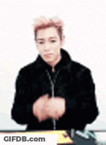 A Man In A Black Jacket Is Sitting At A Table With His Hands Folded In Front Of Him . GIF