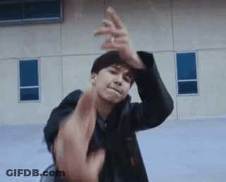 A Man In A Black Jacket Is Sitting In A Chair And Making A Funny Face With His Hands . GIF
