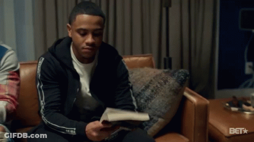 A Man In A Black Jacket Is Sitting On A Couch In A Room . GIF
