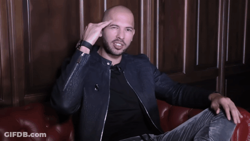 A Man In A Black Jacket Is Sitting On A Red Leather Couch With His Arms Outstretched GIF