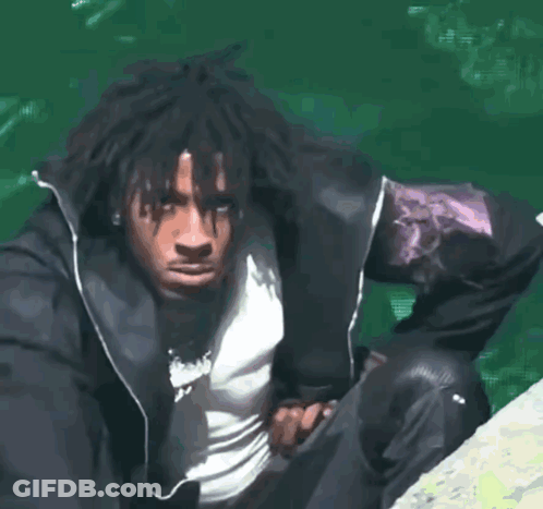 A Man In A Black Jacket Is Sitting On A Rock Near A Body Of Water GIF