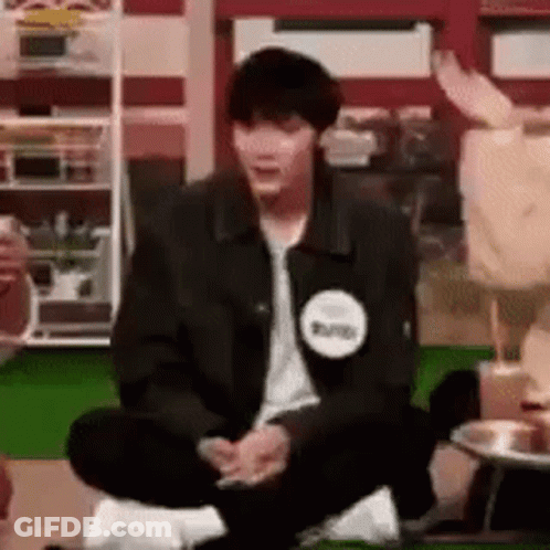A Man In A Black Jacket Is Sitting On The Floor With His Legs Crossed In A Room . GIF