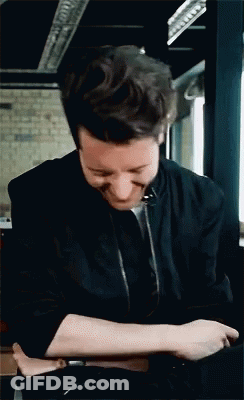 A Man In A Black Jacket Is Smiling And Looking Down GIF